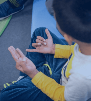 A kid sitting on the floor, counting numbers with his fingers