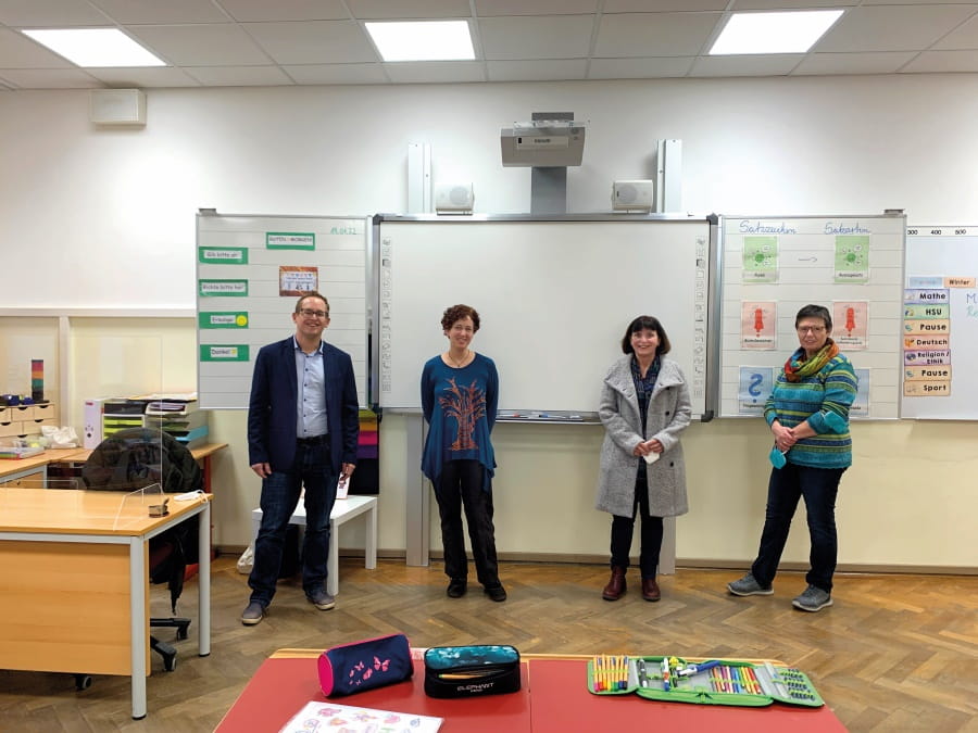 Four teachers in a classroom looking into the camera